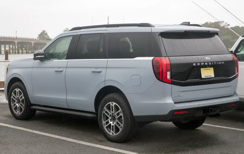 A light gray-blue 2025 Ford Expedition Active parked beside a harbor, seen from the rear left three-quarter angle, its left side and tailgate facing the camera.