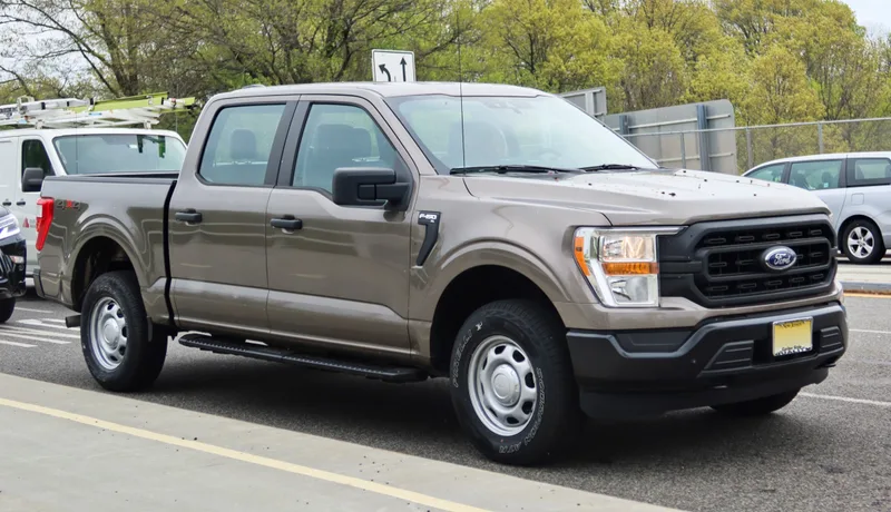 A brown-gray 2021 Ford F-150 XL SuperCrew with steel wheels, seen from the front right three-quarter angle, the same generation as the recalled 2026.