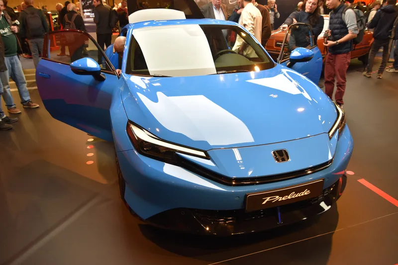 A blue 2026 Honda Prelude, seen from the front, with both doors open, on display at Retromobile 2026 in Paris.