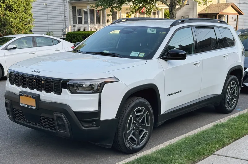A white 2026 Jeep Cherokee Laredo (trim per the Commons file title) parked at a curb, seen from the front left three-quarter angle, its driver's side facing the camera, with Cherokee lettering on the front door.
