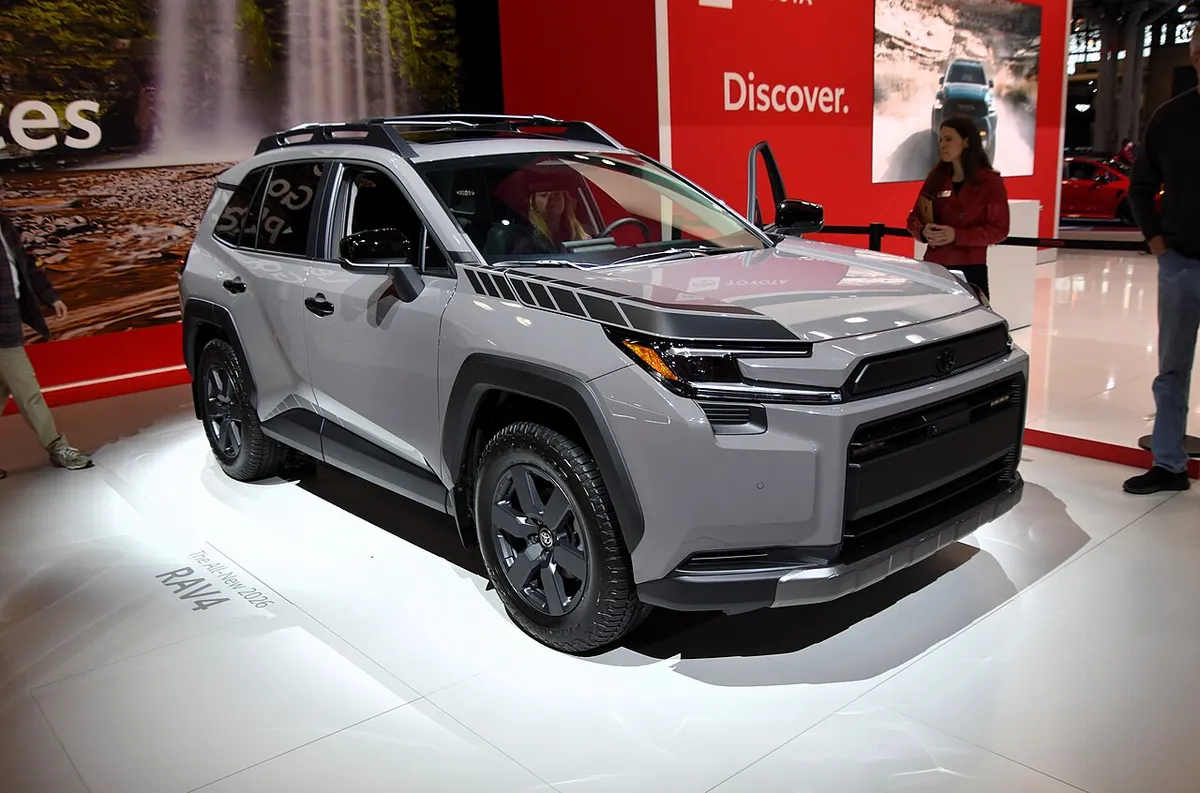 Gray 2026 Toyota RAV4 Woodland Hybrid with a roof rack, front three-quarter view, on an auto show stand.
