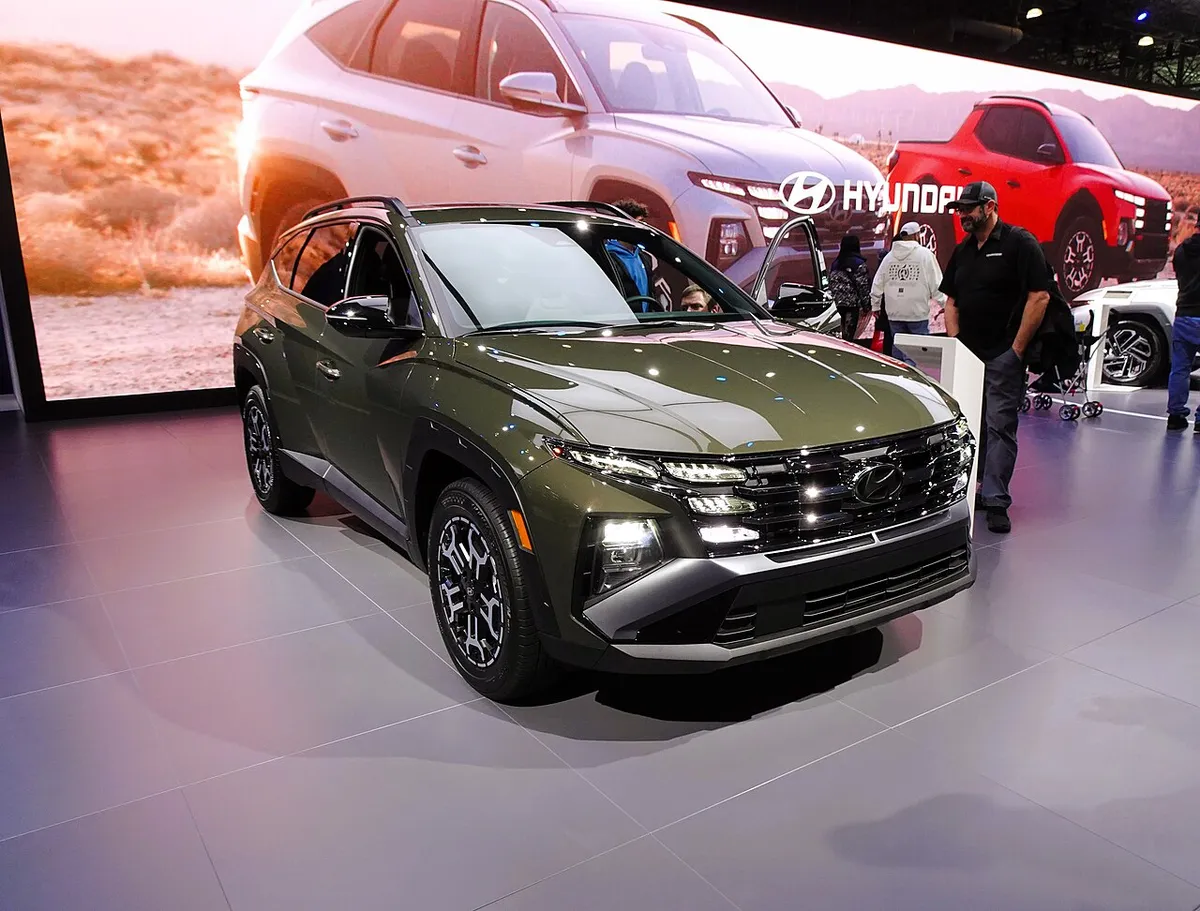 Olive green 2025 Hyundai Tucson XRT on an auto show floor, front three-quarter view.