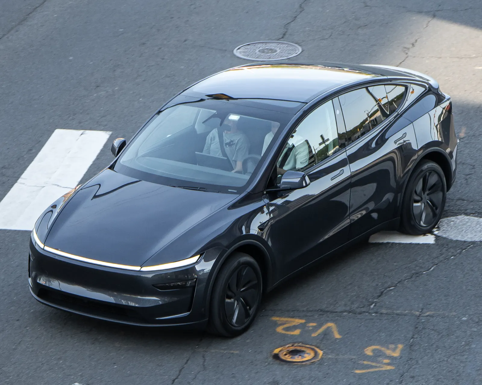 A dark gray Tesla Model Y with the current front-end design, seen from above as it turns through an intersection in the Washington, DC area.