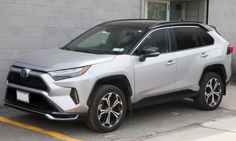 A silver 2024 Toyota RAV4 Prime XSE with a black roof parked on a New York street, seen from the front left (driver's side) at a three-quarter angle. It is the 2024 plug-in RAV4 sold as the RAV4 Prime, not a 2026 vehicle from the recall.